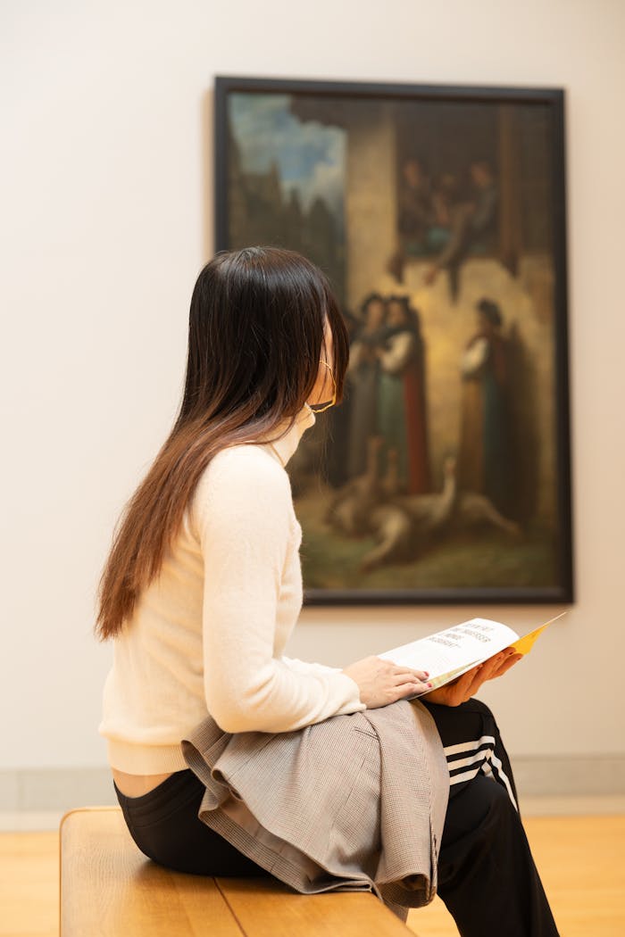 Woman sitting in a contemporary art gallery, observing a painting, holding a brochure.