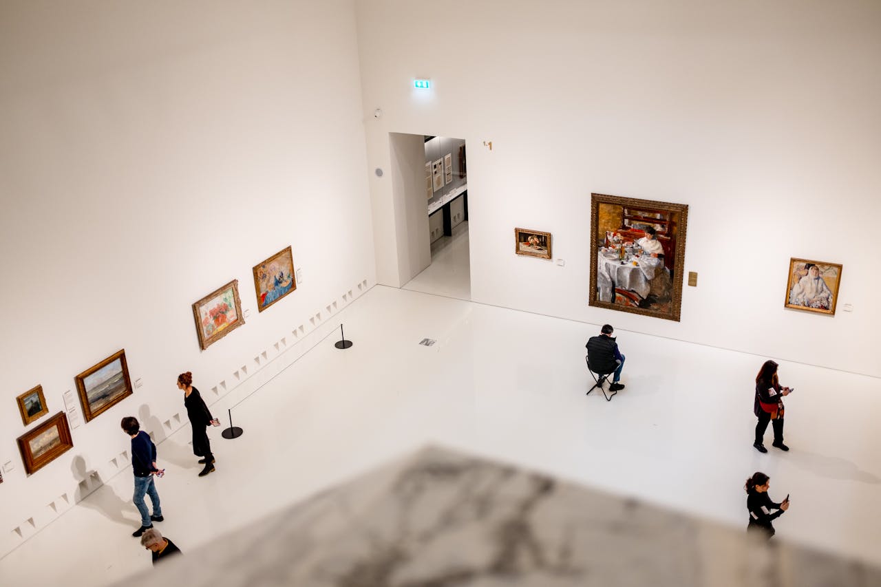 About Visitors exploring an art gallery with various paintings on display from a high angle view.