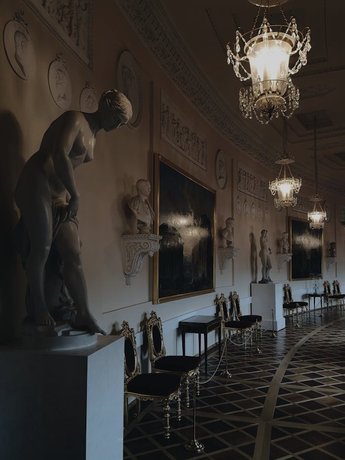 Services A dimly lit museum hall showcasing classic sculptures, ornate chairs, and elegant chandeliers.
